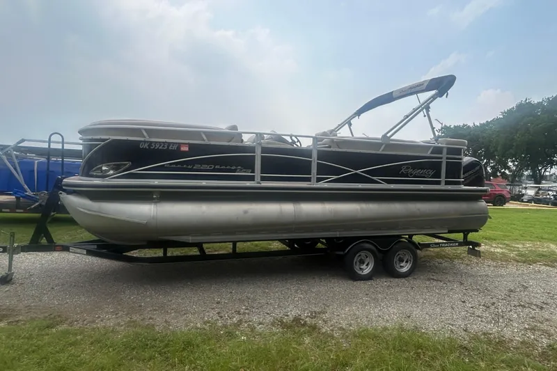 The Image of 2014 Regency 220 DL3 pontoon boat on trailer, parked on gravel. - 1