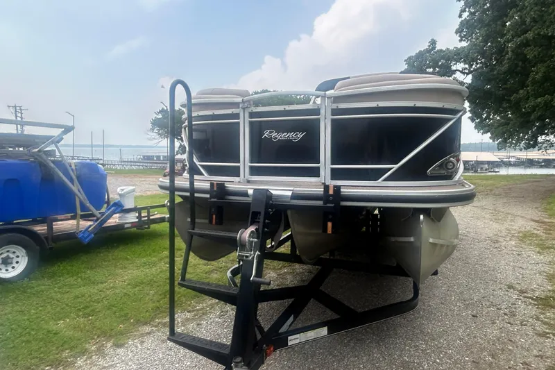 Slide: The Image of 2014 Regency 220 DL3 pontoon boat on trailer near a lake. - 3