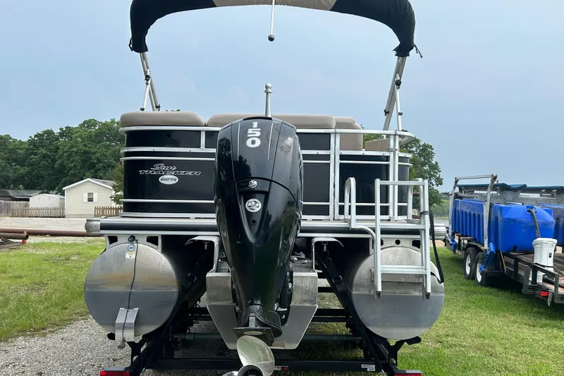 Slide: The Image of 2014 Regency 220 DL3 pontoon boat with outboard motor, parked on grass. - 4