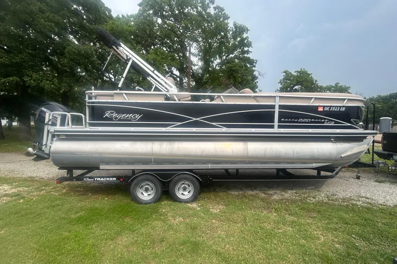 Slide: The Image of 2014 Regency 220 DL3 pontoon boat on trailer, parked on grass with trees in background. - 6