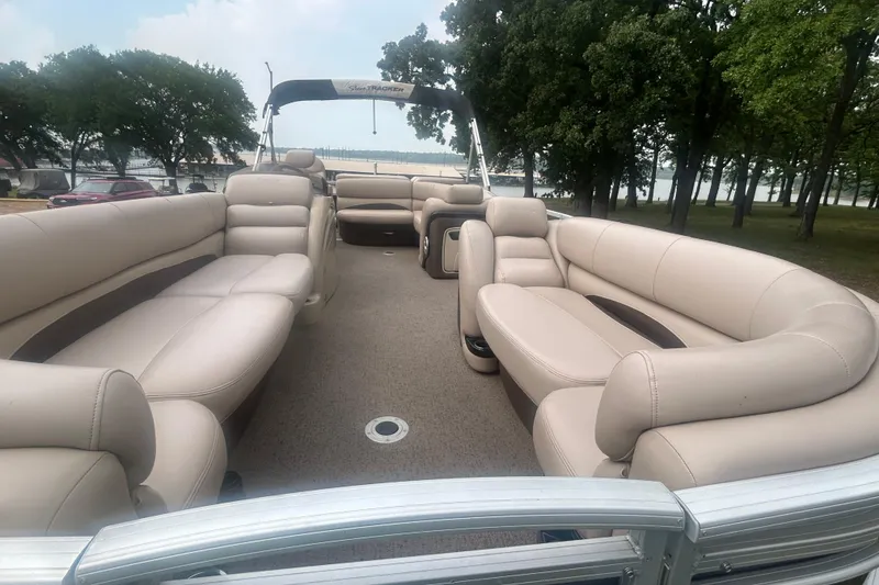 Slide: The Image of 2014 Regency 220 DL3 pontoon boat with spacious beige seating, docked near trees. - 7