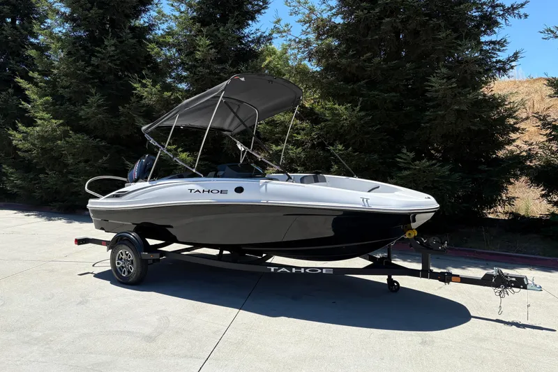 Slide: The Image of 2026 Tahoe T16 boat on trailer, parked outdoors with trees in background. - 2