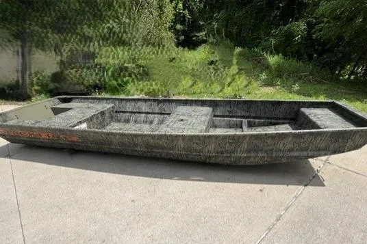The Image of 2026 Tracker Grizzly 15 Jon boat on concrete, surrounded by greenery. - 0