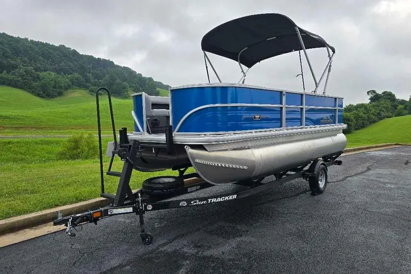 Slide: The Image of 2026 Sun Tracker Party Barge 18 DLX pontoon boat on trailer, parked on asphalt. - 1