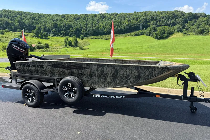The Image of 2026 Tracker Grizzly 1650 T Prairie Wings Edition boat on trailer, scenic green landscape. - 0
