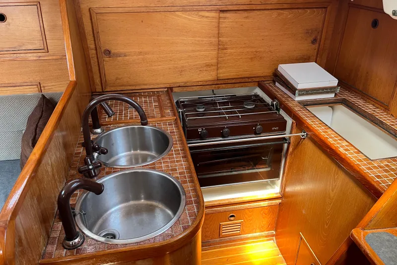 Slide: The Image of 1986 Wauquiez Petorine yacht kitchen with dual sinks and stove, featuring wooden cabinetry. - 7