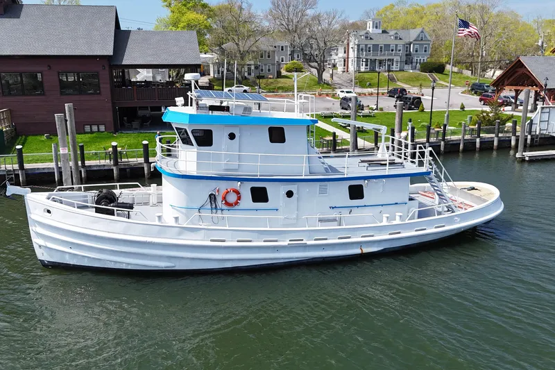 Slide: The Image of 1954 American 70 Tugboat docked by waterfront buildings and greenery. - 4