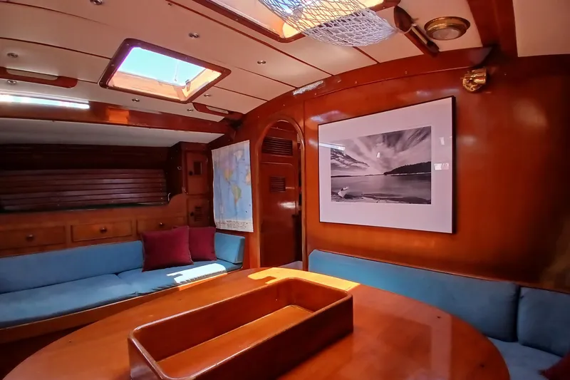 Slide: The Image of Cozy 1981 SKYE 51 yacht interior with wooden decor, blue seating, and nautical artwork. - 18