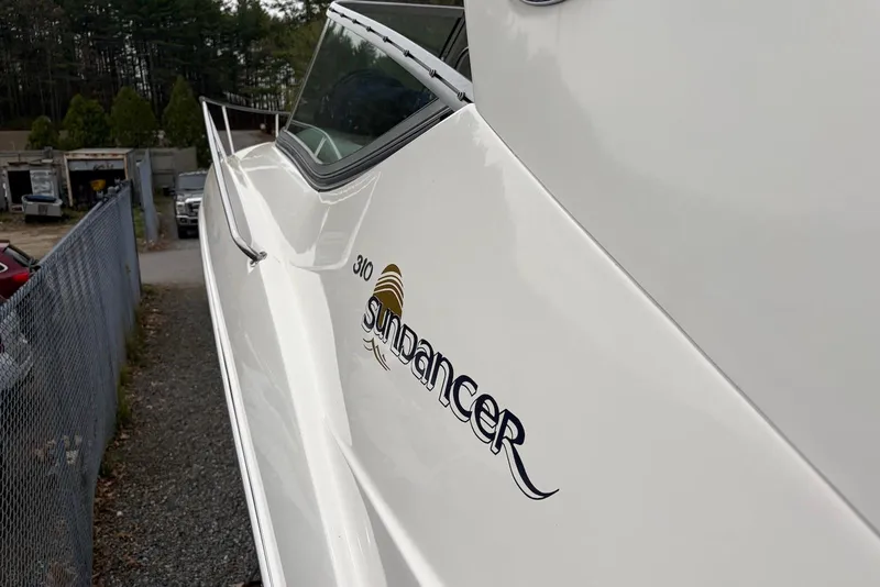 Slide: The Image of 2008 Sea Ray Sundancer 310 boat side view with logo, parked near a fence. - 7