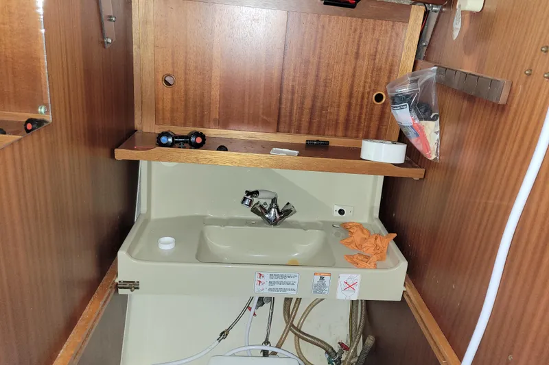 Slide: The Image of Small boat bathroom sink with wooden cabinetry, plumbing visible, and repair tools. LM 32, 1986 model. - 27