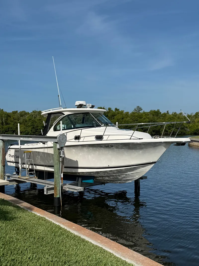 The Image of 2011 Pursuit 315 OS boat on a lift dock by the water. - 0