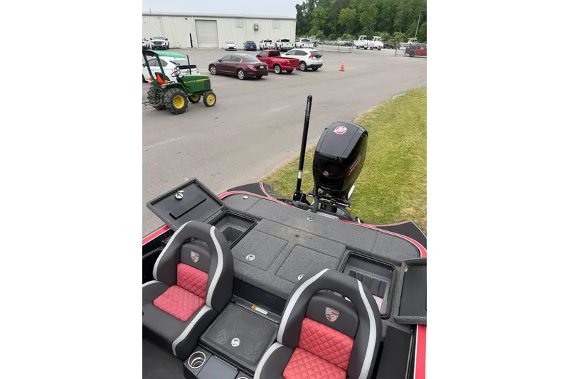 Slide: The Image of 2022 Triton 18 TrX boat with red and black seating, parked near vehicles and a tractor. - 7
