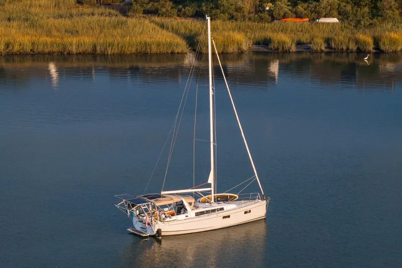 The Image of 2018 Beneteau Oceanis 38.1 sailboat anchored on calm water near lush shoreline. - 0