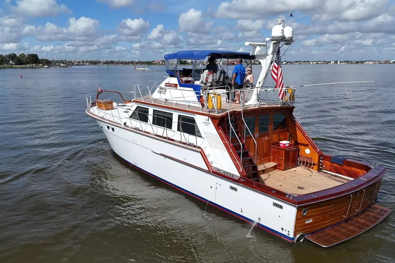 Slide: The Image of 1980 Bertram 58 Convertible yacht cruising on a calm, scenic waterway under a cloudy sky. - 2