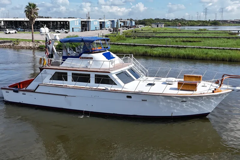 Slide: The Image of 1980 Bertram 58 Convertible yacht cruising on a calm river under a clear blue sky. - 4
