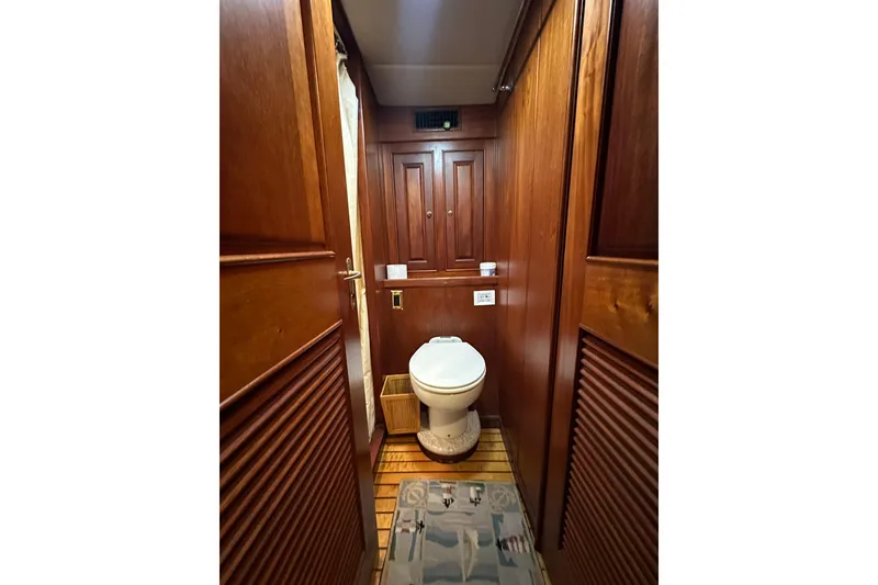 Slide: The Image of Wood-paneled bathroom interior of 1980 Bertram 58 Convertible yacht, featuring a toilet and storage cabinets. - 62