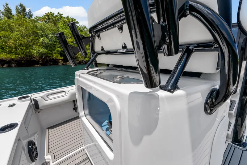 Slide: The Image of 2026 Tidewater 2500 Carolina Bay boat interior with rod holders and storage, near lush shoreline. - 20