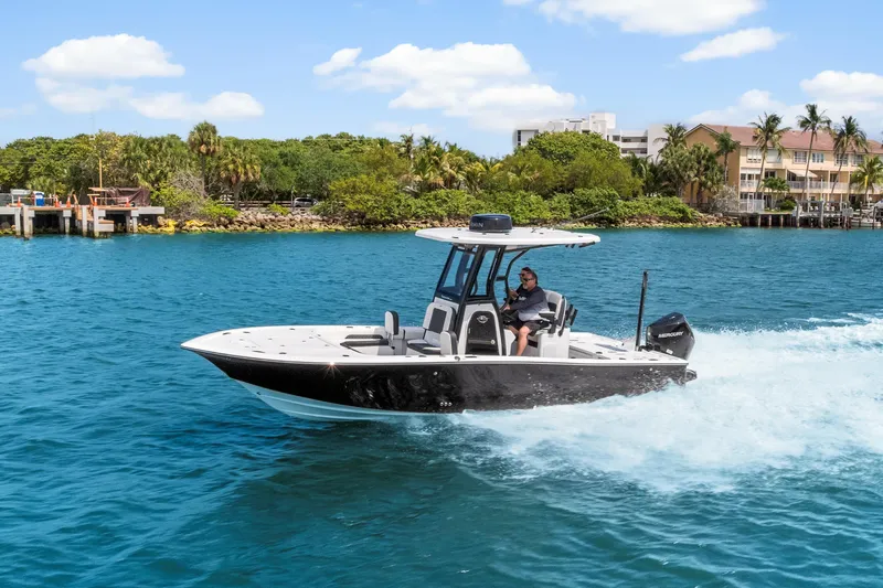 Slide: The Image of 2026 Tidewater 2500 Carolina Bay boat cruising on clear blue water near lush shoreline. - 3