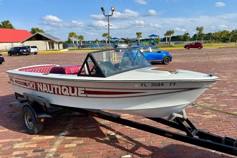 Slide: The Image of 1981 SKI NAUTIQUE boat on trailer, parked in sunny lot with red and blue cars nearby. - 14