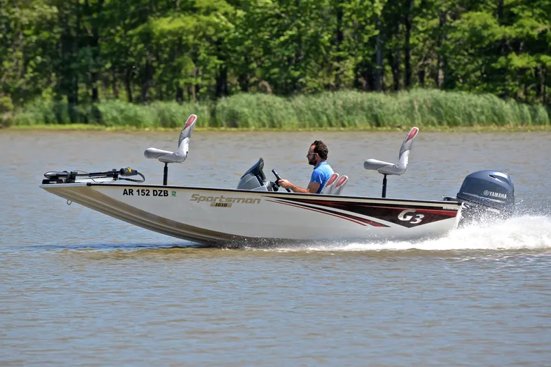 Slide: The Image of 2023 G3 Sportsman 1610 boat cruising on a lake with lush green background. - 2