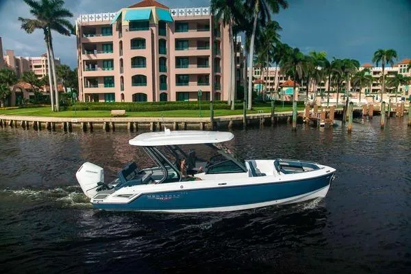 The Image of 2027 Monterey Elite 27 OB boat cruising near waterfront buildings and palm trees. - 0
