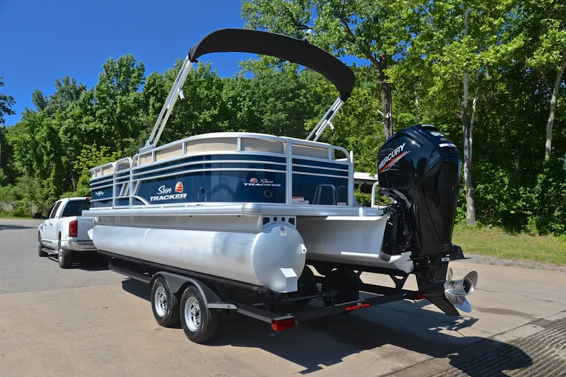 Slide: The Image of 2022 Sun Tracker Party Barge 20 DLX pontoon boat on trailer, parked near trees. - 12