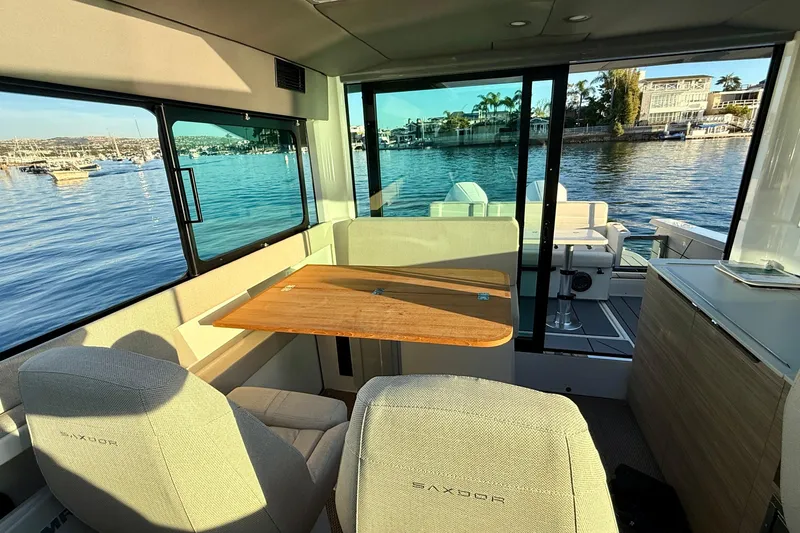 Slide: The Image of Interior of 2025 Saxdor 320 GTC boat with seating and table, overlooking a scenic waterfront. - 26