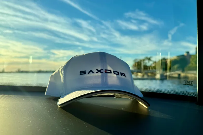 Slide: The Image of White Saxdor cap on dashboard, scenic waterfront view, Saxdor 320 GTC, 2025 model. - 39