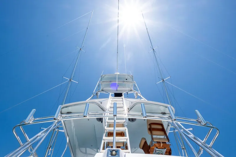 Slide: The Image of 1998 Hatteras 60 Convertible yacht under bright sun, showcasing sleek design and tall masts. - 29