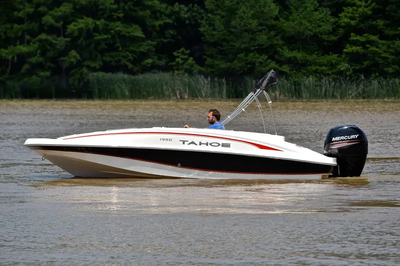 Slide: The Image of A 2018 Tahoe 1950 boat cruising on a lake with lush green trees in the background. - 9