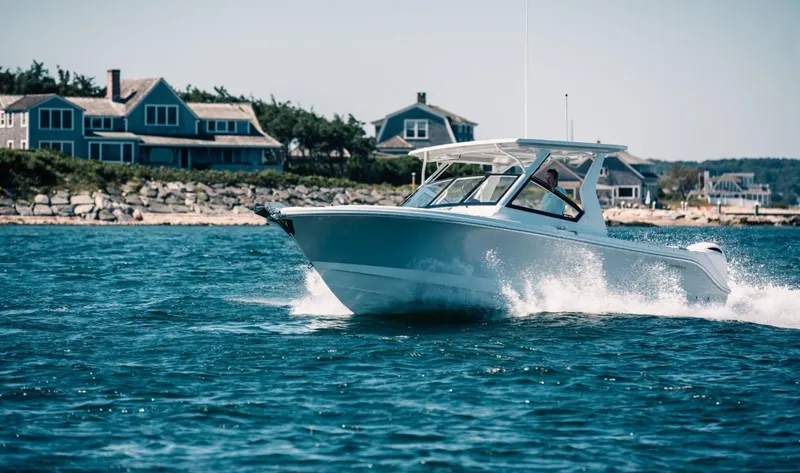 The Image of Edgewater 262 CX 2025 boat cruising near coastal homes on a sunny day. - 0