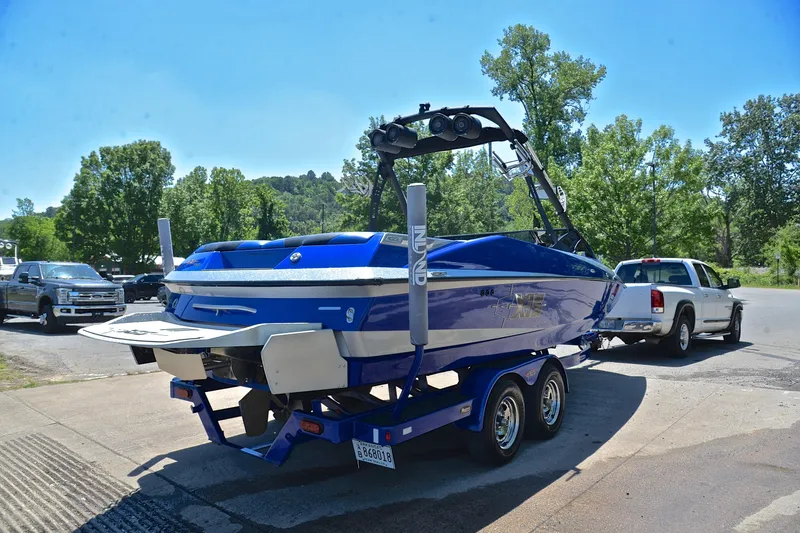 Slide: The Image of 2014 Axis A22 boat on trailer, blue and white, parked near trees and vehicles. - 14