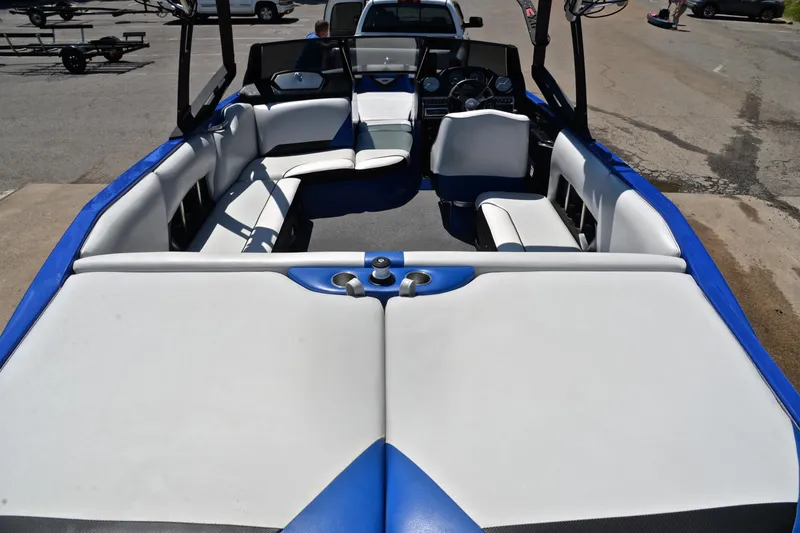 Slide: The Image of 2014 Axis A22 boat interior with white and blue seating, parked on a sunny day. - 18