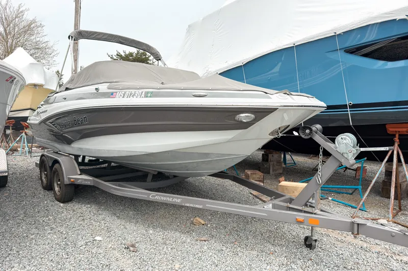 Slide: The Image of 2018 Crownline Eclipse E215 XS boat on trailer, covered and parked on gravel. - 1
