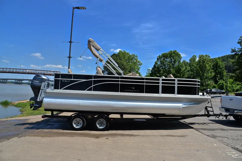 Slide: The Image of 2019 Bennington 22 pontoon boat on trailer by a river, under clear blue sky. - 15