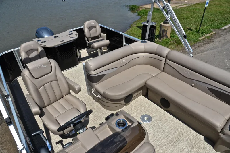 Slide: The Image of 2019 Bennington 22 pontoon boat interior with beige seating and steering console by the water. - 23