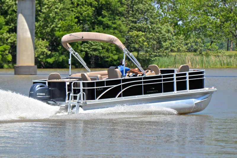 Slide: The Image of 2019 Bennington 22 pontoon boat cruising on a lake with lush greenery. - 5