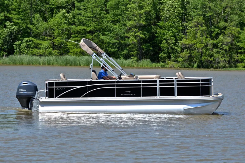 Slide: The Image of 2019 Bennington 22 pontoon boat cruising on a lake with lush green forest backdrop. - 6