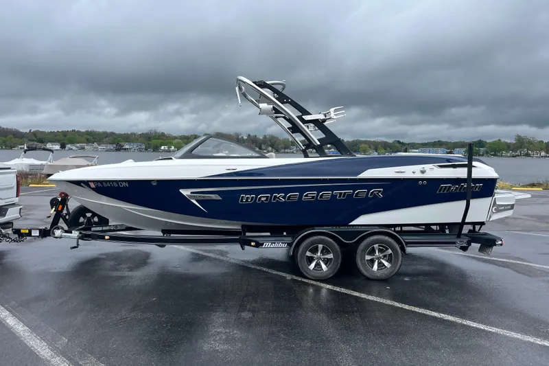 Slide: The Image of 2014 Malibu Wakesetter 23 LSV boat on trailer, parked near a lake under cloudy skies. - 9