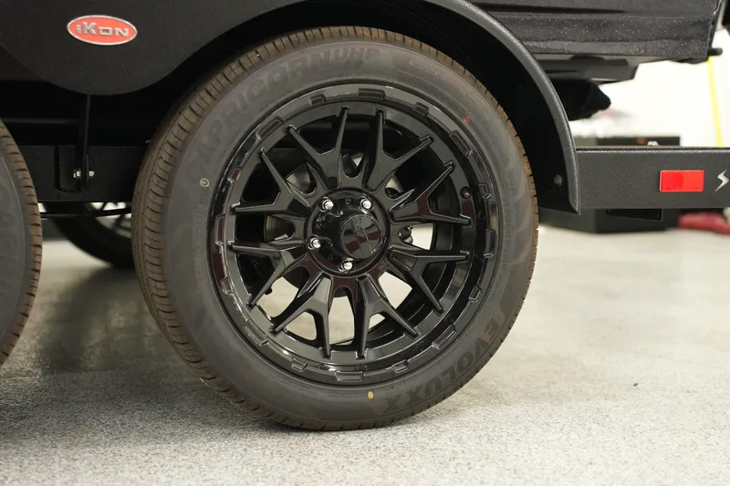 Slide: The Image of Black alloy wheel of 2026 iKon LXE20 vehicle on a showroom floor. - 3