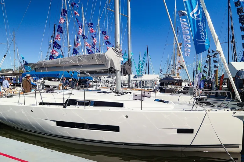 Slide: The Image of Modern Hanse 360 sailboat from 2026 displayed at a boat show, surrounded by flags. - 1