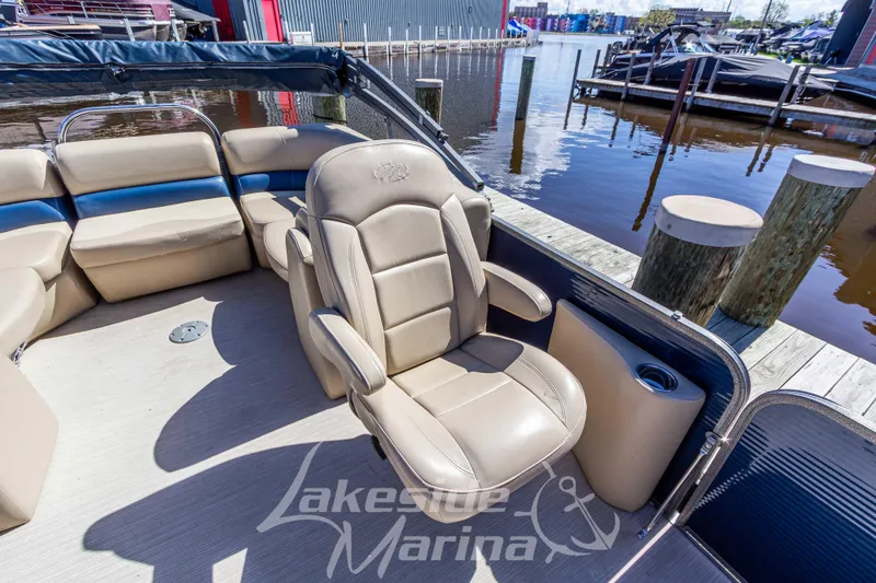 Slide: The Image of 2018 Manitou Aurora 23 LE RF VP boat interior with beige seating at a marina. - 13