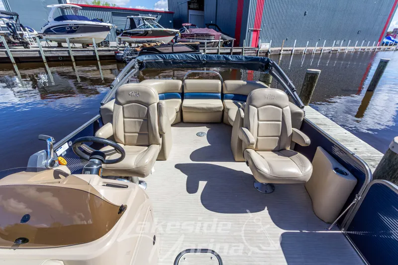 Slide: The Image of 2018 Manitou Aurora 23 LE RF VP pontoon boat interior with beige seating at a marina. - 9