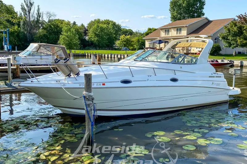 Slide: The Image of 1998 Cruisers Yachts 2870 Rogue docked on a serene lake with lush greenery. - 2