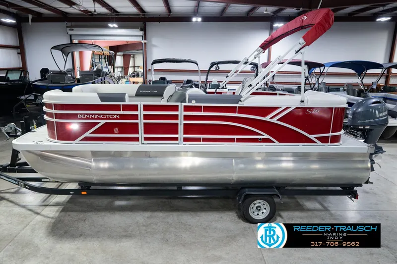 The Image of 2025 Bennington 20 SLS pontoon boat with red accents, displayed indoors on a trailer. - 1