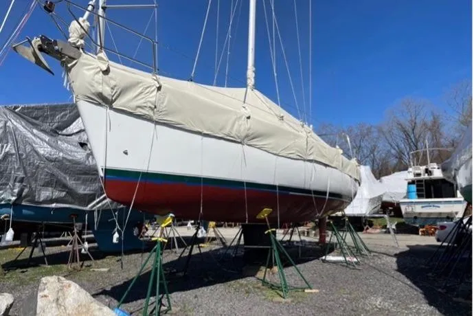 Slide: The Image of 2003 Beneteau 423 sailboat on stands, covered, in a boatyard under clear blue sky. - 8