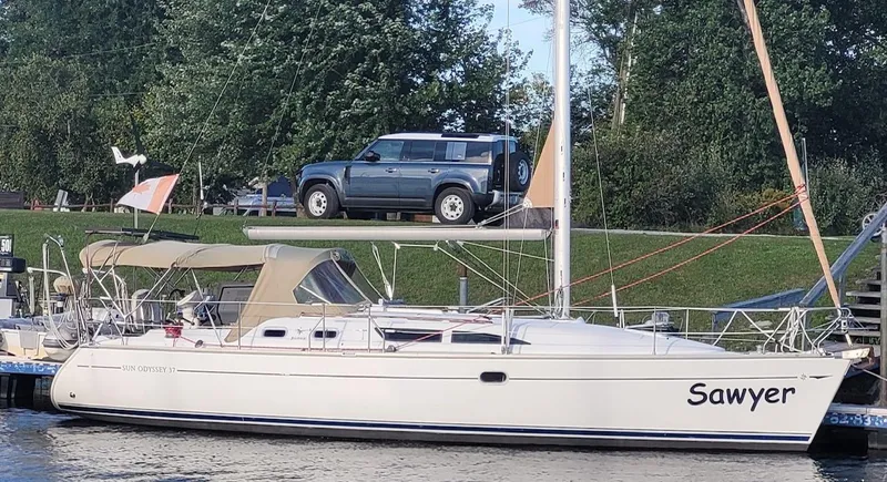 Slide: The Image of 2004 Jeanneau SO 37 sailboat named "Sawyer" docked near a grassy shoreline. - 2