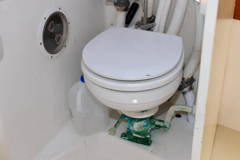 Slide: The Image of Marine toilet in a 1993 Freya 39 sailboat bathroom, with plumbing and a water jug. - 55