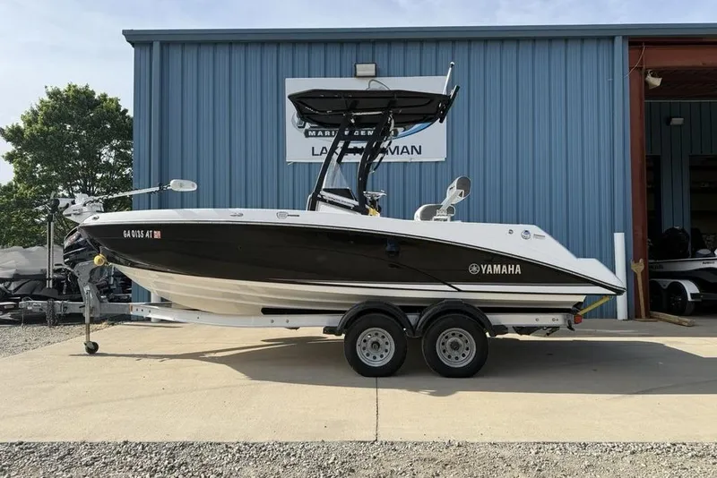 The Image of 2020 Yamaha Boats 210 FSH Sport on trailer outside blue building. - 1