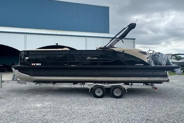 Slide: The Image of 2020 Barletta Lusso 25QCSS pontoon boat on trailer, parked near a blue warehouse. - 8
